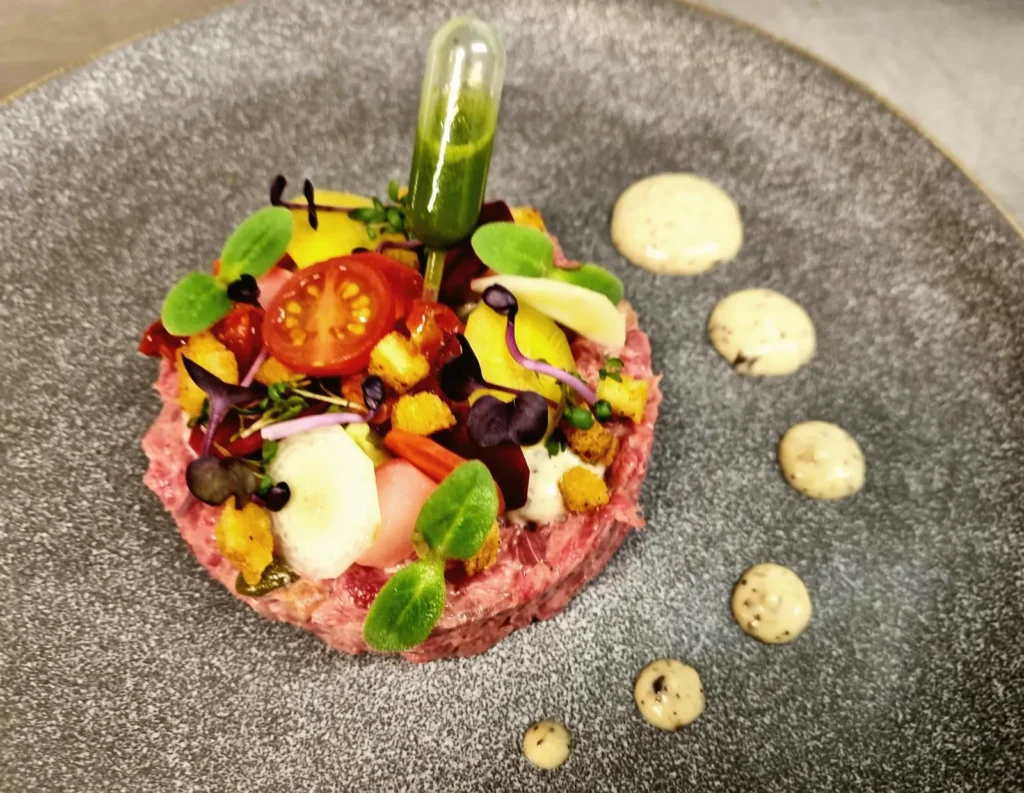 Tartaar met kerstomaat, groenten, kruiden en stippen saus op een grijs bord