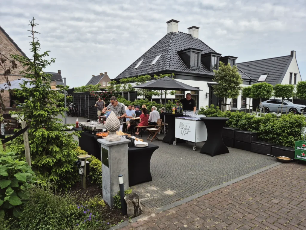 Tuinfeest met gasten aan statafels bij een buffet onder parasols